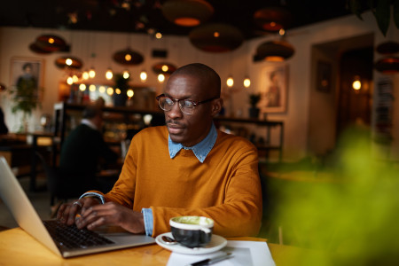 Man wearing orange jumper, using laptop in cafe.