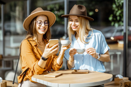 Two women sat together, looking at a mobile phone, in a cafe.