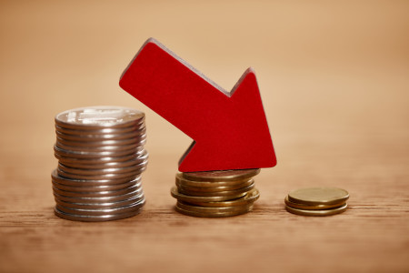 a red arrow going down, on top of piles of coins.