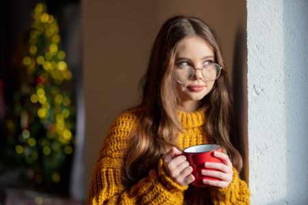 Girl wearing yellow sweater and glasses, holding a mug.