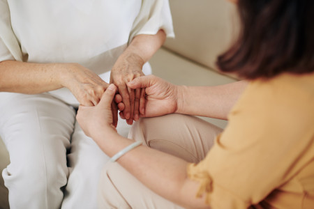 Woman wearing a yellow top, reassuring another person, by holding their hands.