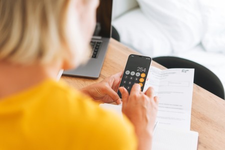 Woman, wearing yellow sweater, looking at calculator on her phone.