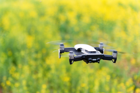 Drone flying over a green field with yellow flowers.