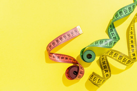 Three colourful measuring tapes on a yellow background.