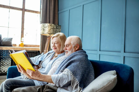 Old couple reading a book on a sofa.