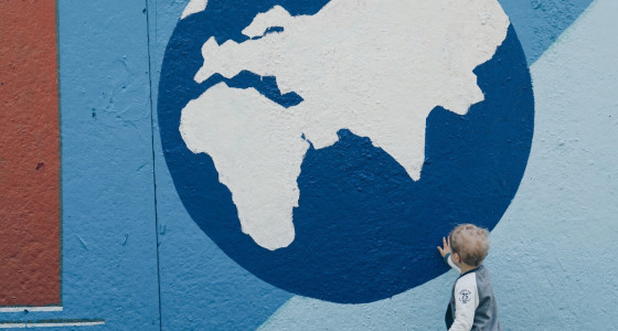 Small child facing a big picture of the globe on a blue wall