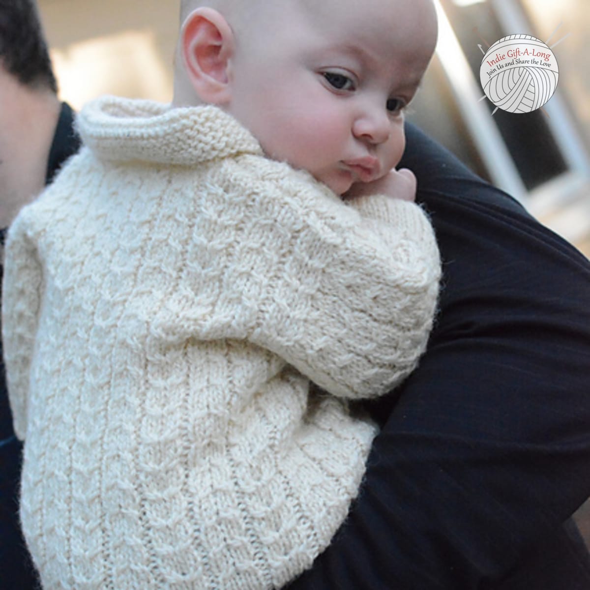 Baby wearing white knitted cardigan with cable details.