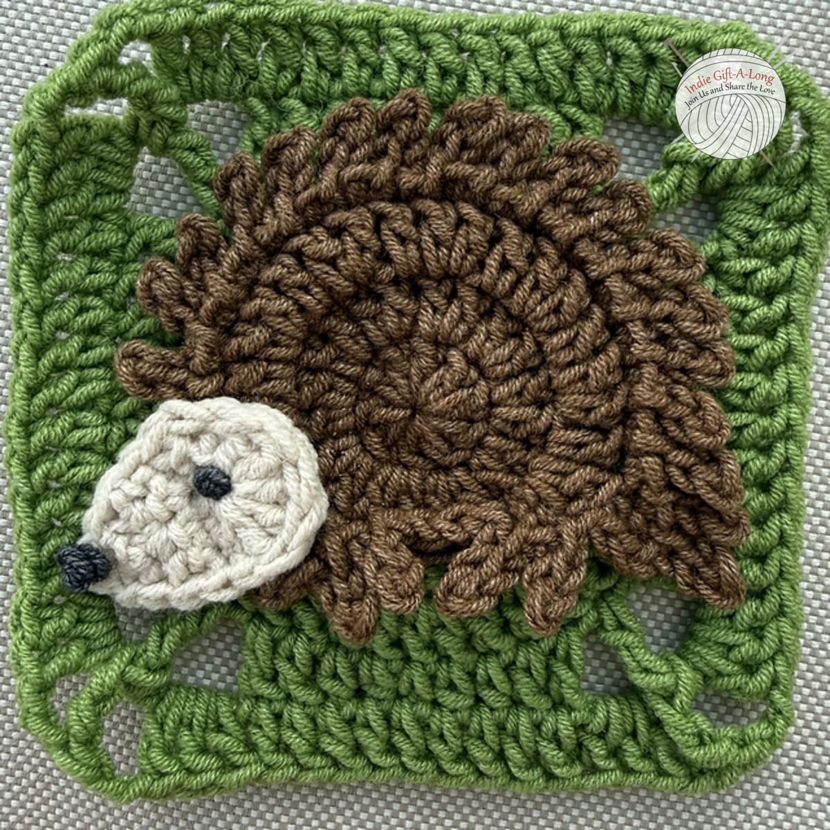 Green crocheted square with brown hedgehog motif.