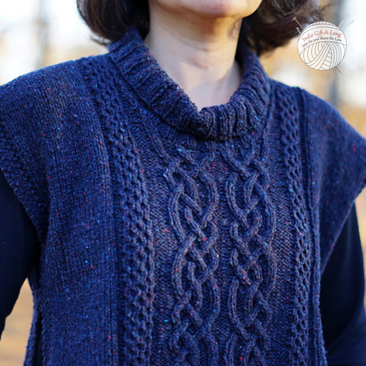 Woman wearing blue knitted poncho with turtleneck and cable motif.