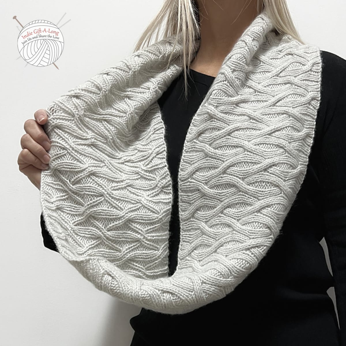 Woman wearing white knitted cowl with reversible cable motif.