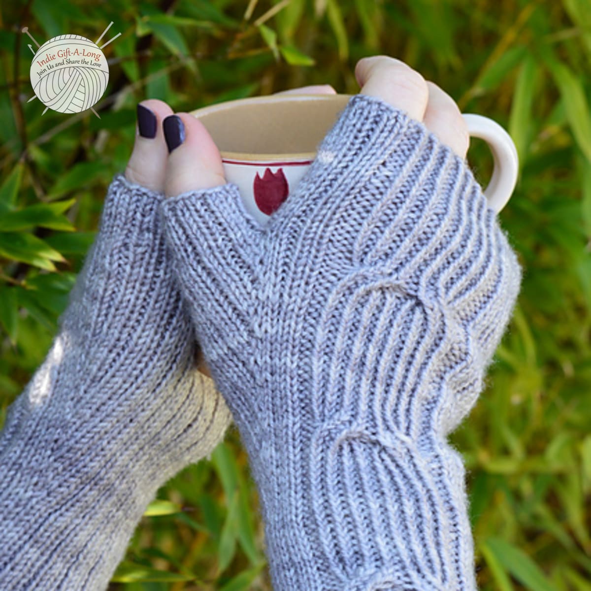 Hands holding mug and wearing light grey knitted fingerless mitts with subtle cable details.