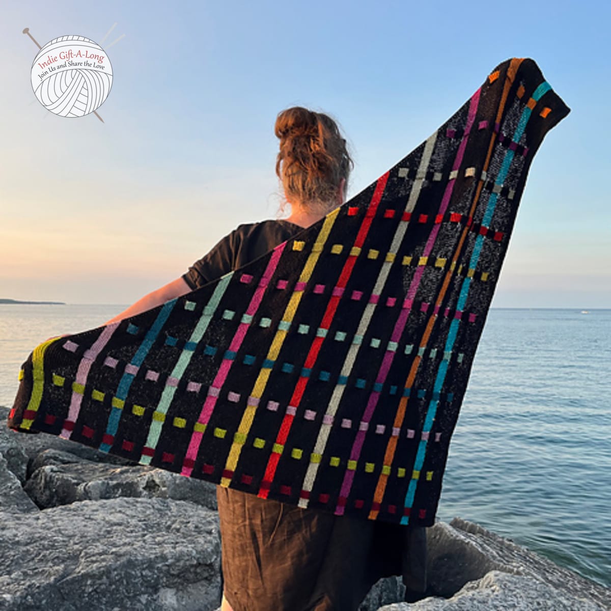 Woman holding black knitted shawl with rainbow lines and squares.