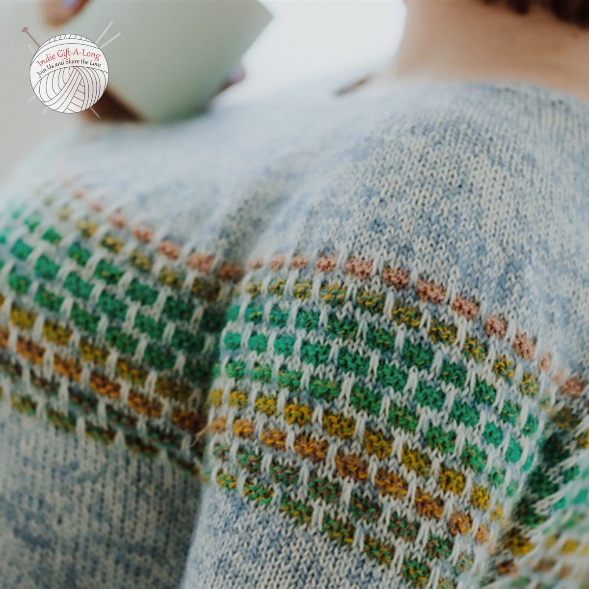 Close up of grey knitted sweater with green and brown brickwork-inspired motif detailing.