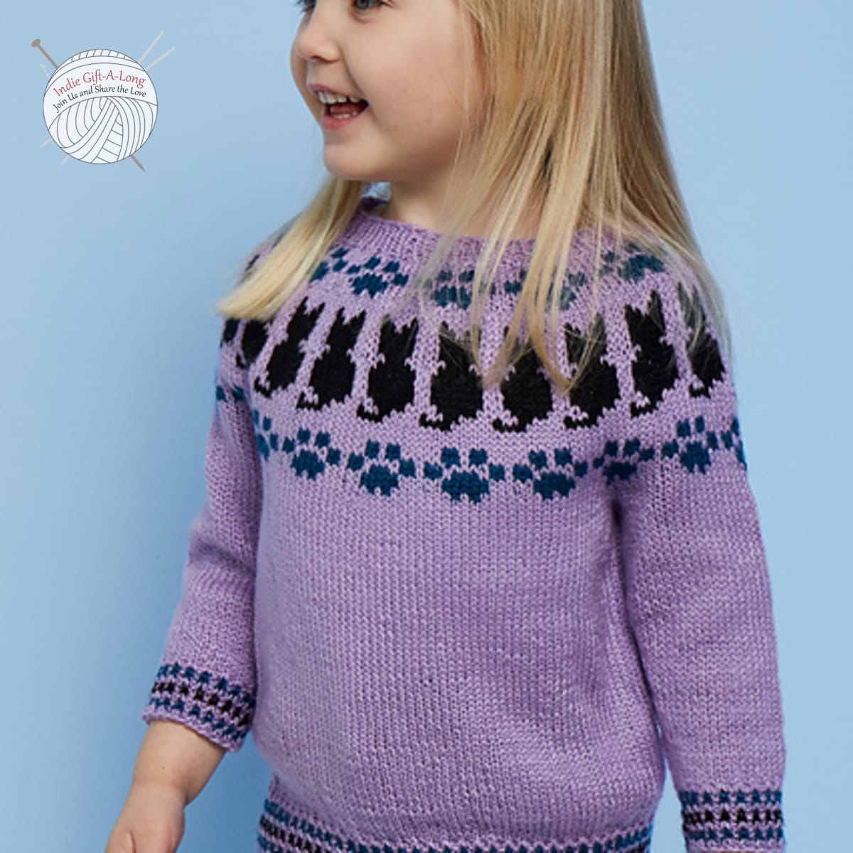 Child wearing purple knitted sweater with cat-themed motifs.