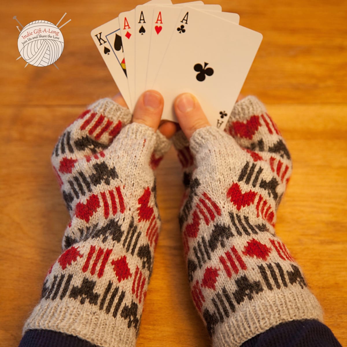 Hands wearing knitted fingerless mitts with hearts, spades, diamonds, and clubs motifs.