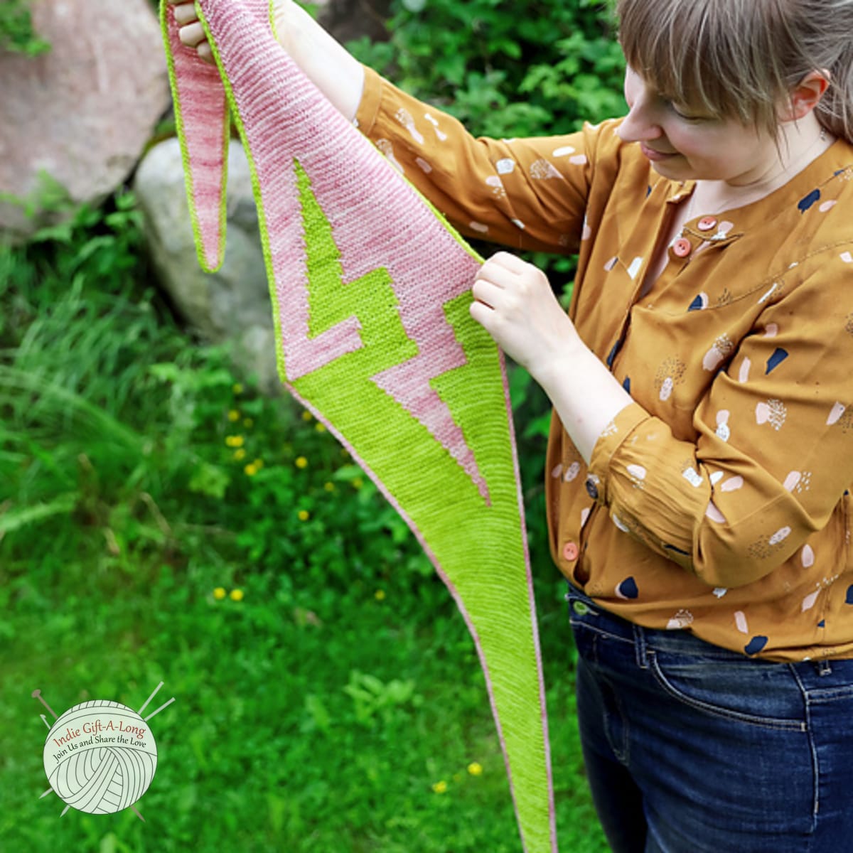 Hands holding light green and pink knitted scarf with zigzag motif.
