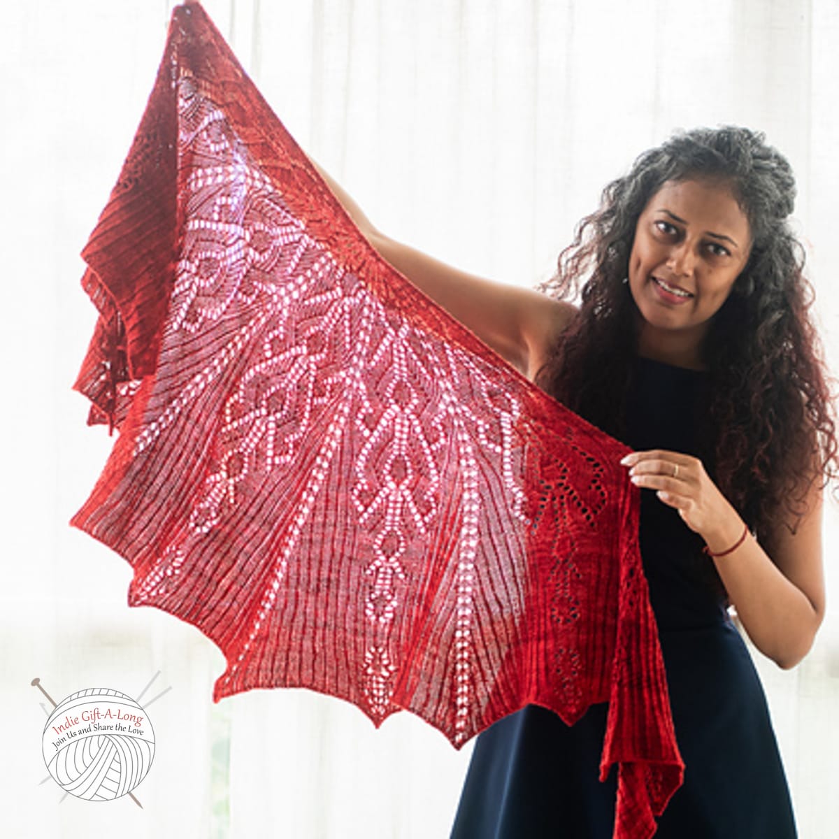 Woman holding red knitted shawl with geometric lace motif.