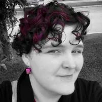 Black and white photo of a woman with pops of pink in her hair and on her earrings.