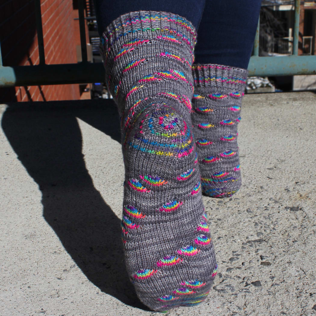 Back view of grey socks with rainbow oval sections and textured cuffs and heels.