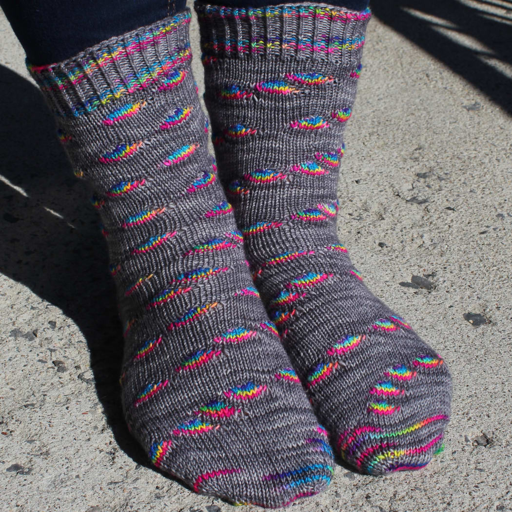 Front view of grey socks with rainbow oval sections and textured cuffs and heels.