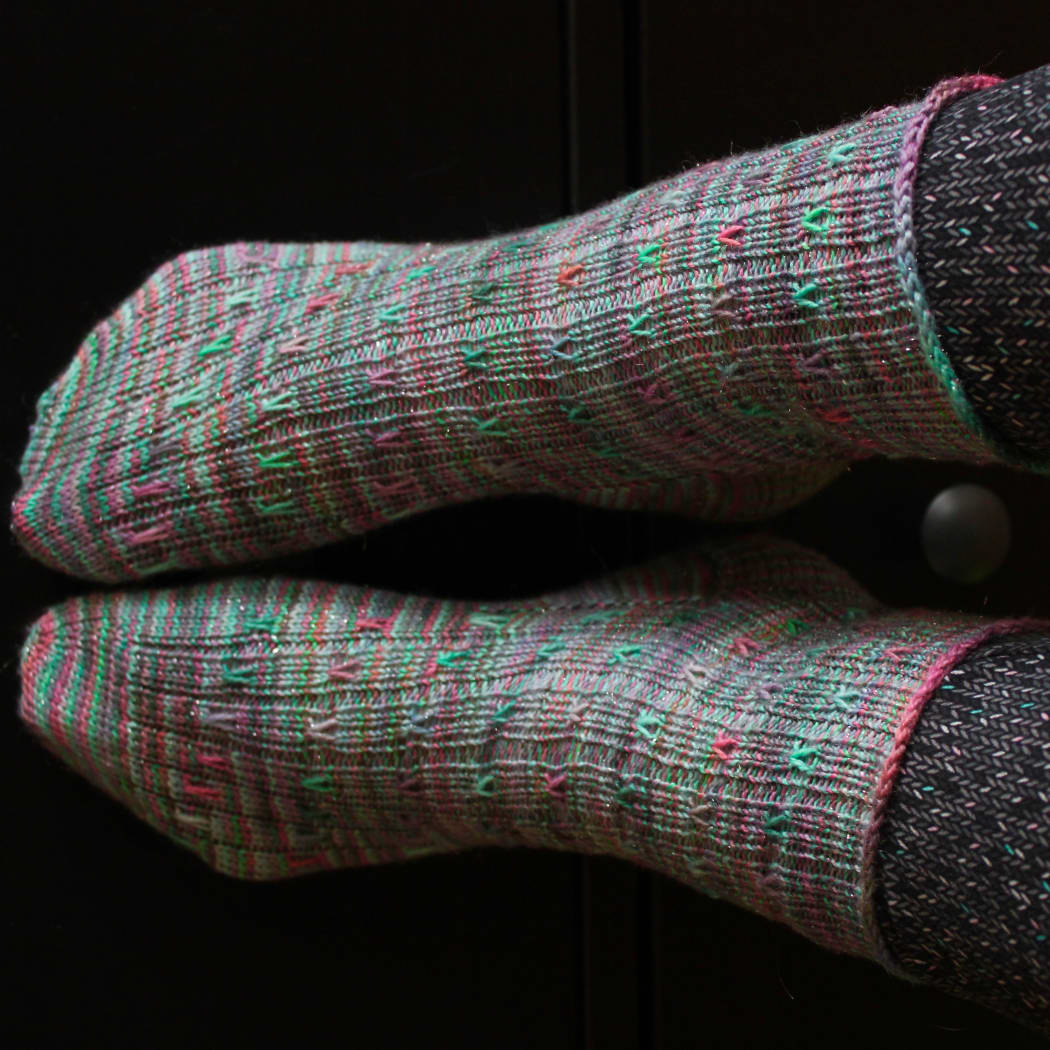 Feet wearing green ribbed socks with coral and purple spiralling surface detail.