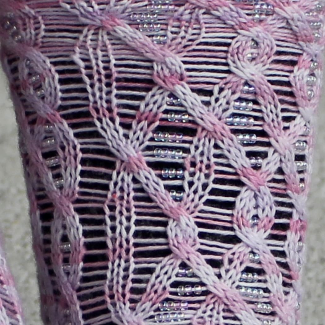 Close up of light pink cabled socks with beads on strands between the cable crosses.