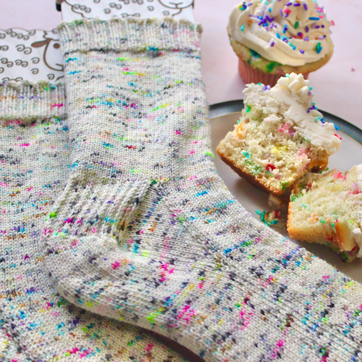 Close view of rainbow speckled socks on sock blockers beside a plate of rainbow-speckled cupcakes.