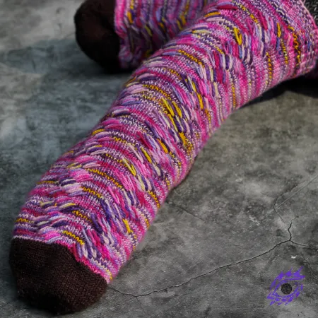 Feet wearing pink, yellow, and purple knitted socks with mirrored diagonal lines of stacked elongated stitches.