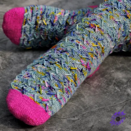 Close up of feet wearing blue, pink, and yellow knitted socks with zigzags of elongated stitches.