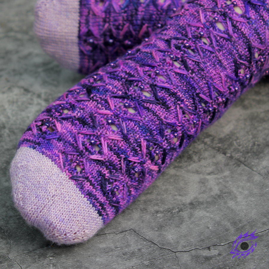 Close up of feet wearing neon purple knitted socks with zigzags of elongated stitches with subtle lace accents and shiny purple beads.