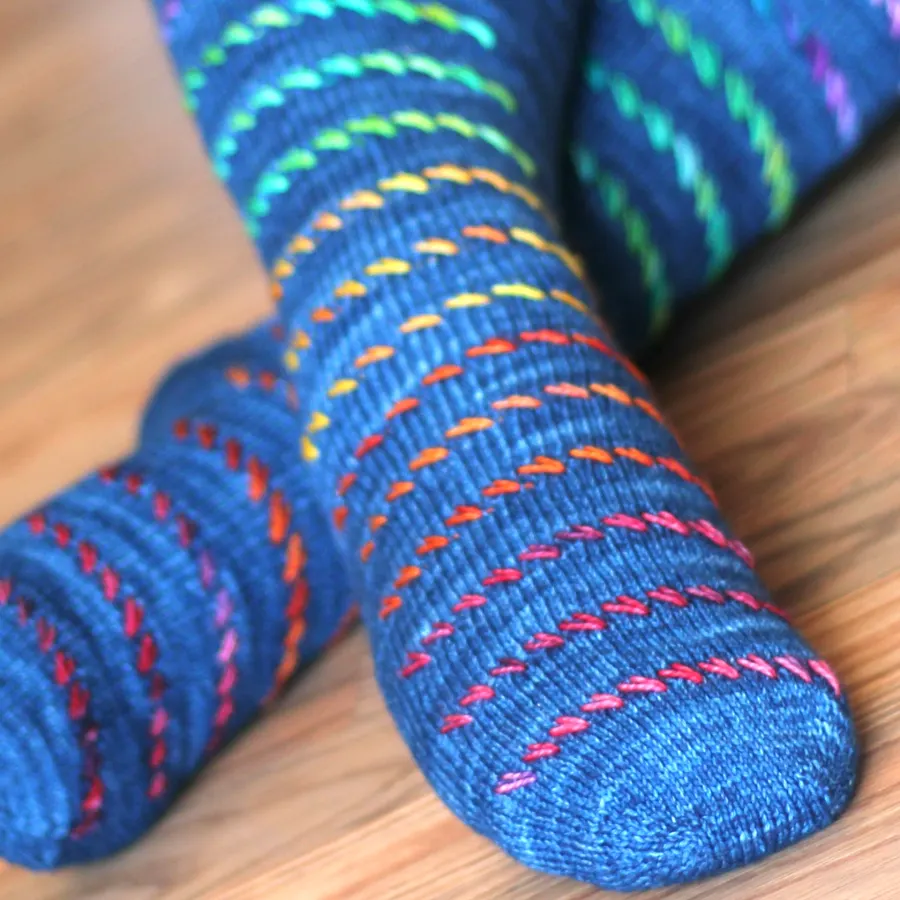 Crossed feet wearing blue socks with rainbow diagonal surface texture.