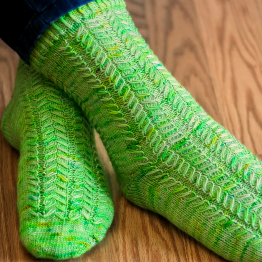Close view of crossed feet wearing green socks with mirrored slipped-stitch cable surface texture.