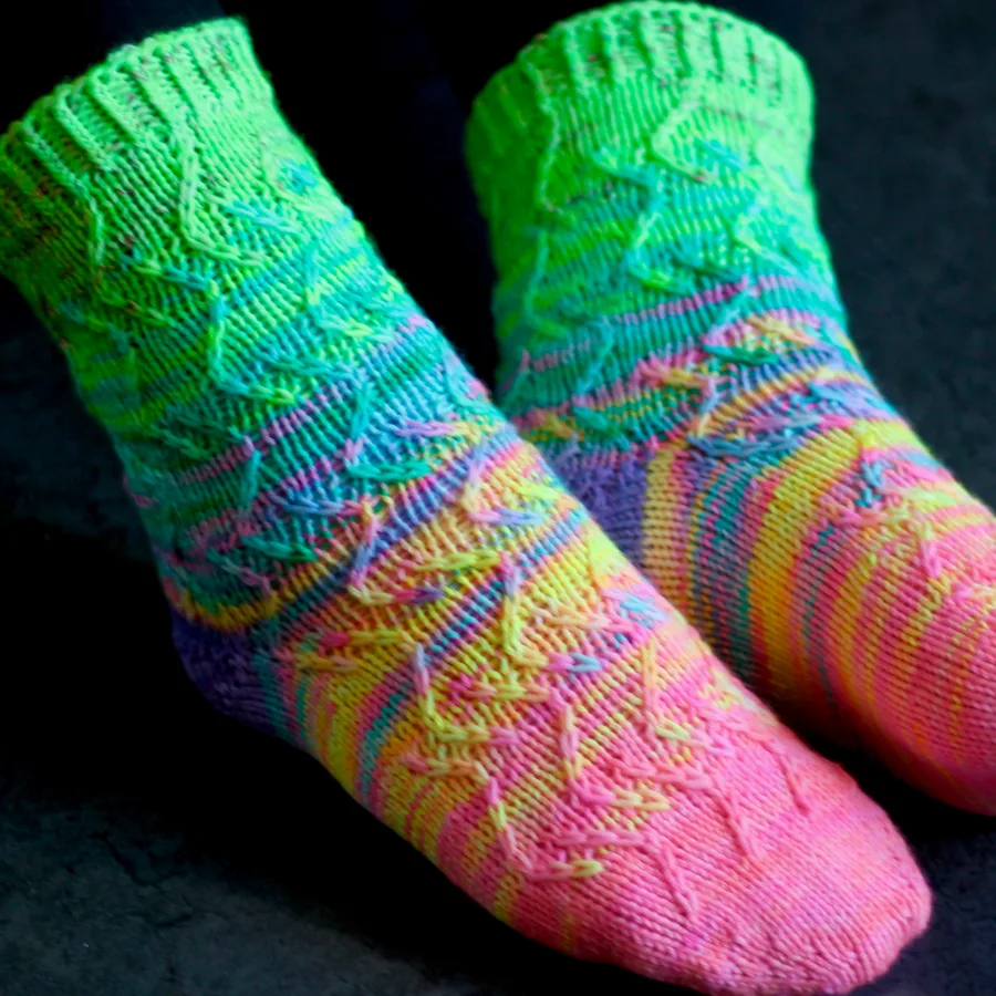 Side view of feet wearing neon rainbow socks with zigzag surface texture and purple heel.