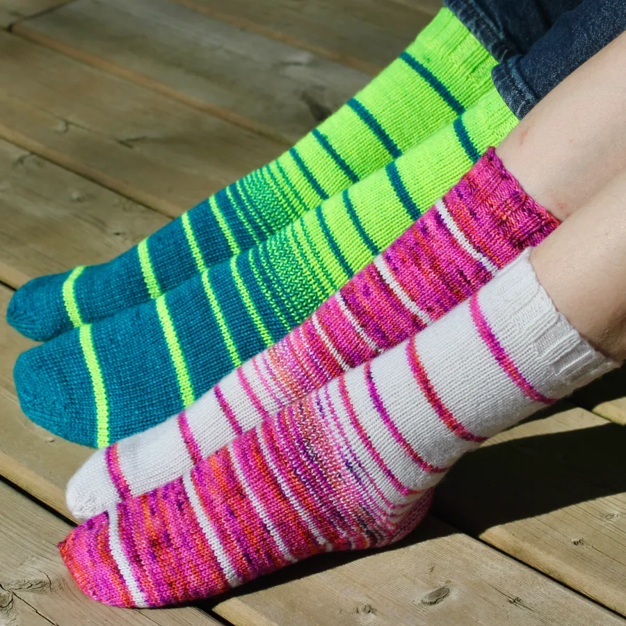 Side view of two pairs of feet wearing knitted socks in a variable-width striping pattern.