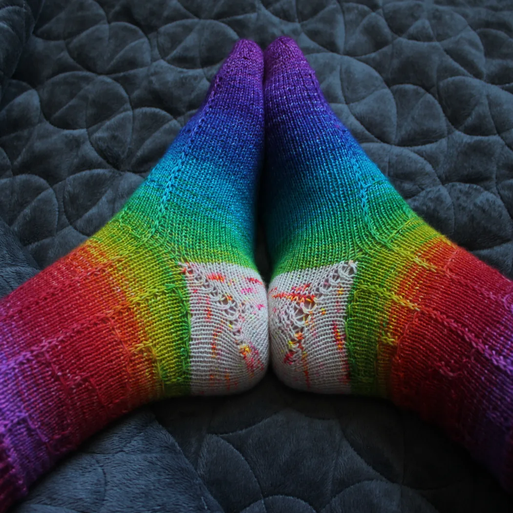 Side view of rainbow socks with subtle surface detail and white, orange, yellow, and pink speckled heels.