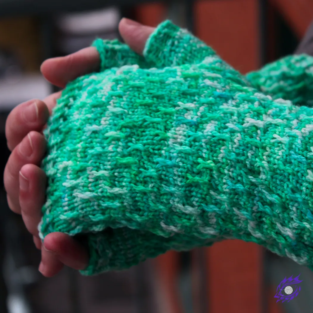 Side view of hands held together wearing bright green, white, and blue fingerless mitts with twisted surface detail.