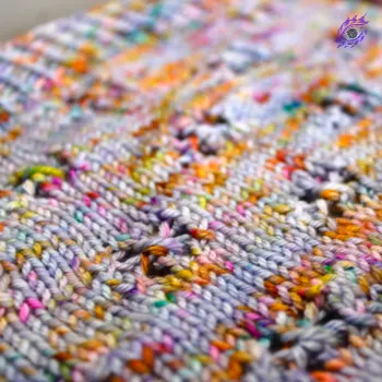 Close up of light purple and rainbow-speckled knitted fabric with lace detail.