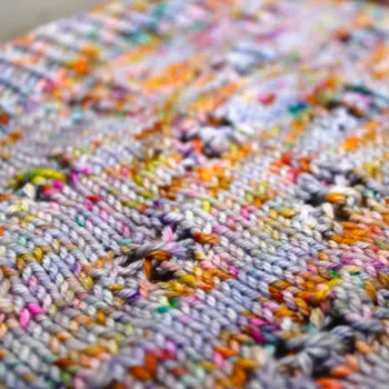 Close up of light purple and rainbow-speckled knitted fabric with lace detail.