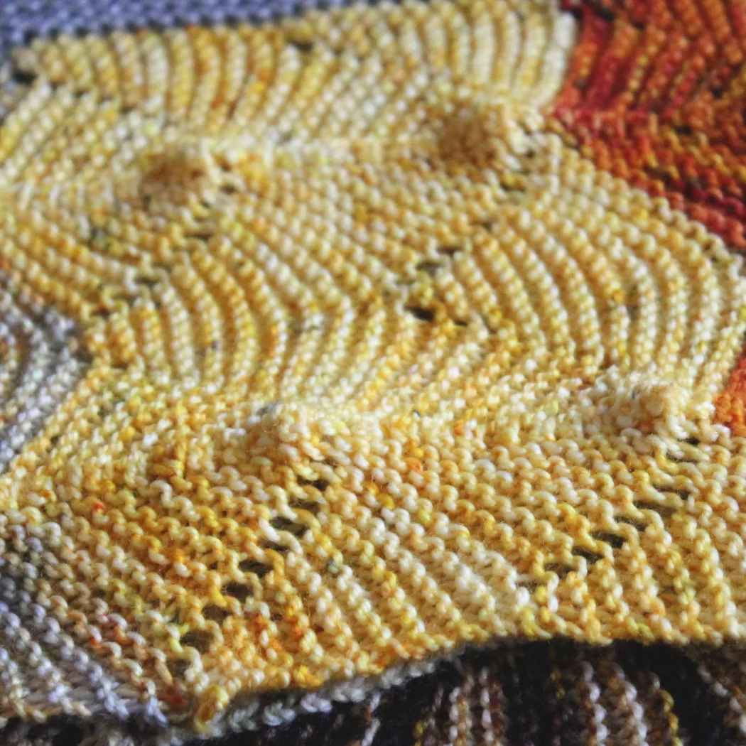 Close up of the edge of a colourful knitted shawl with undulating textured lines.