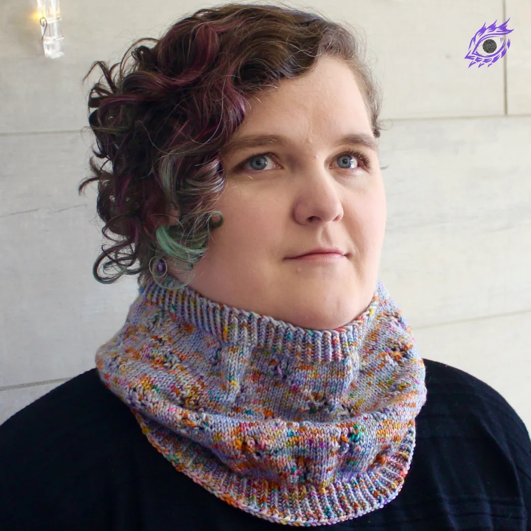 Woman wearing cowl that is light purple and rainbow-speckled knitted fabric with lace detail.