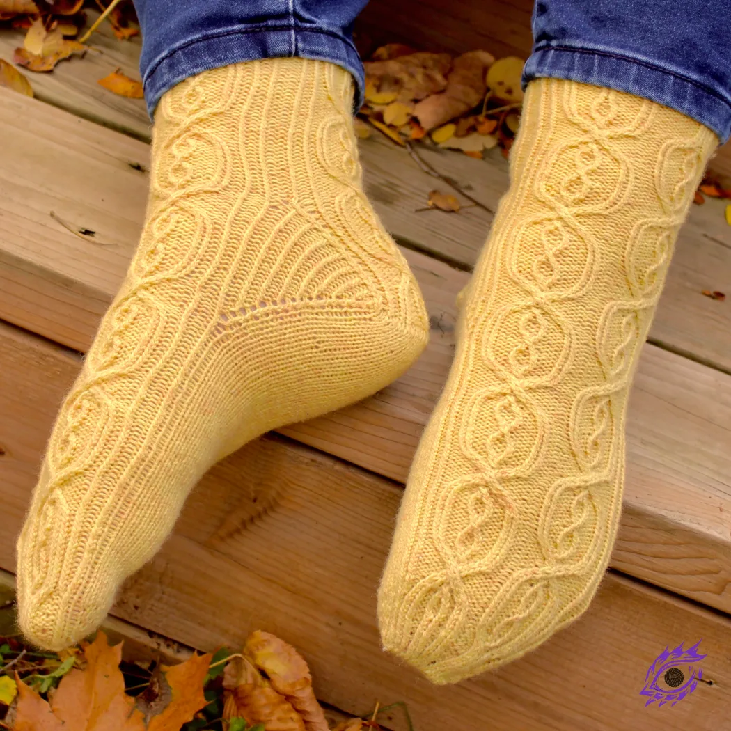 Feet wearing yellow knitted socks with complex cable motif and twisted-rib accents.