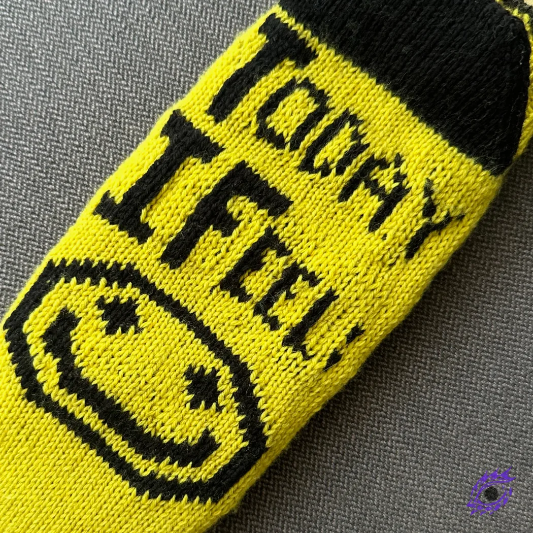 Bottom view of yellow and black knitted socks with graphic happy face motif and text "Today I Feel".