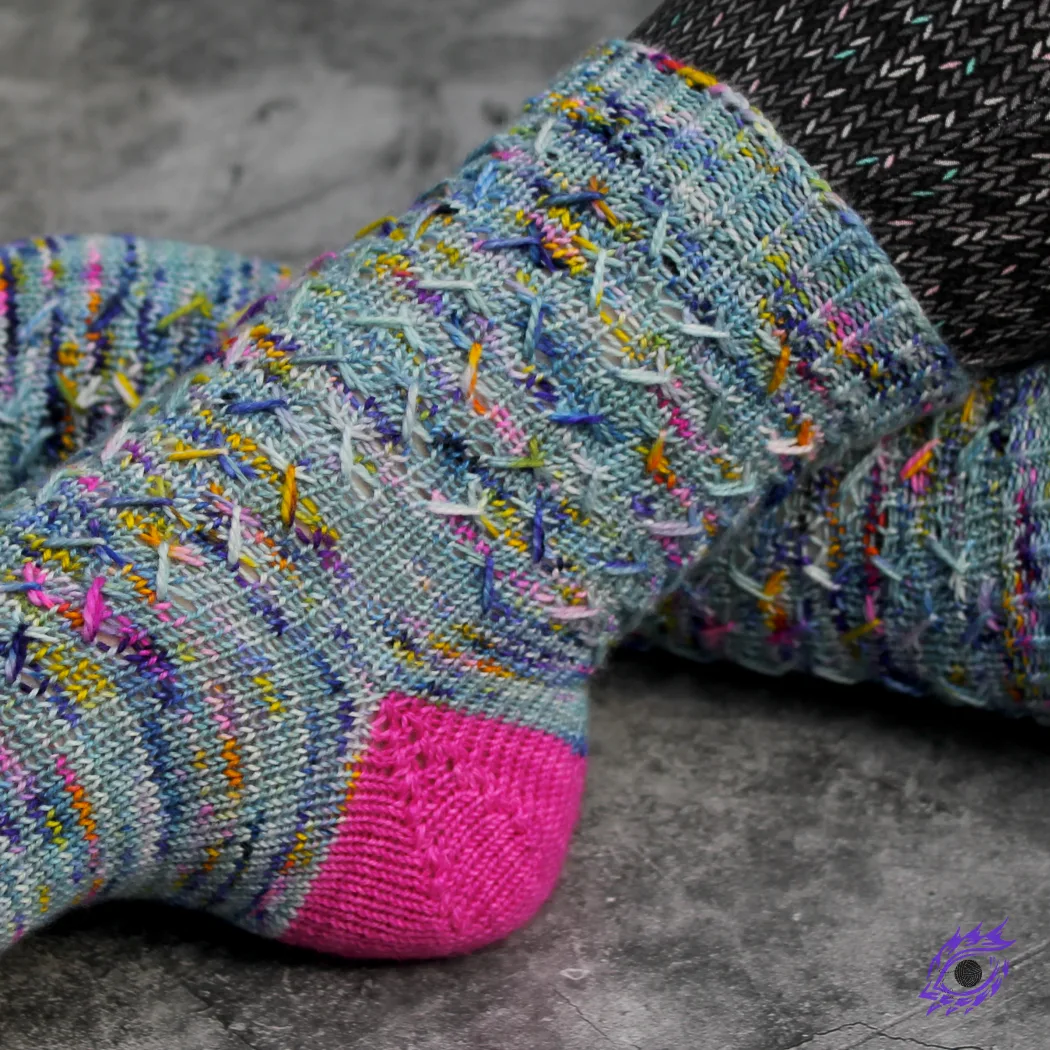 Side view of feet wearing blue, pink, and yellow knitted socks with zigzags of elongated stitches.