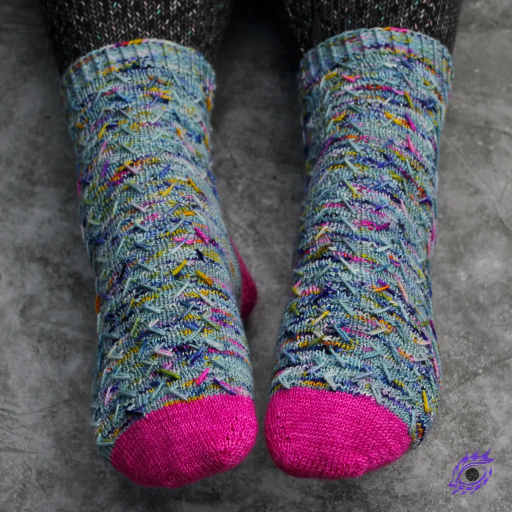 Feet wearing blue, pink, and yellow knitted socks with zigzags of elongated stitches.