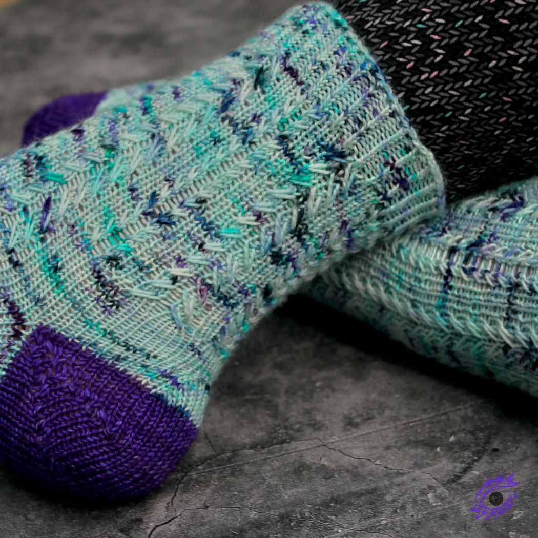Side view of feet wearing blue and purple knitted socks with columns of elongated-stitch cables.