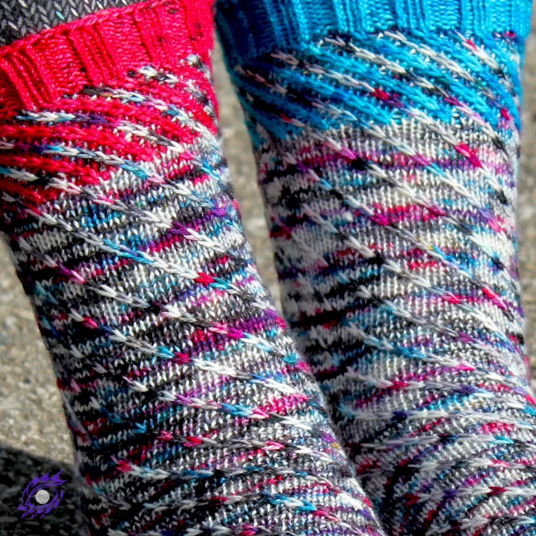 Close up of feet wearing knitted socks in a wildly-speckled yarn with a spiralling slipped-stitch texture; the socks have diagonal accent-colour sections at the cuffs.