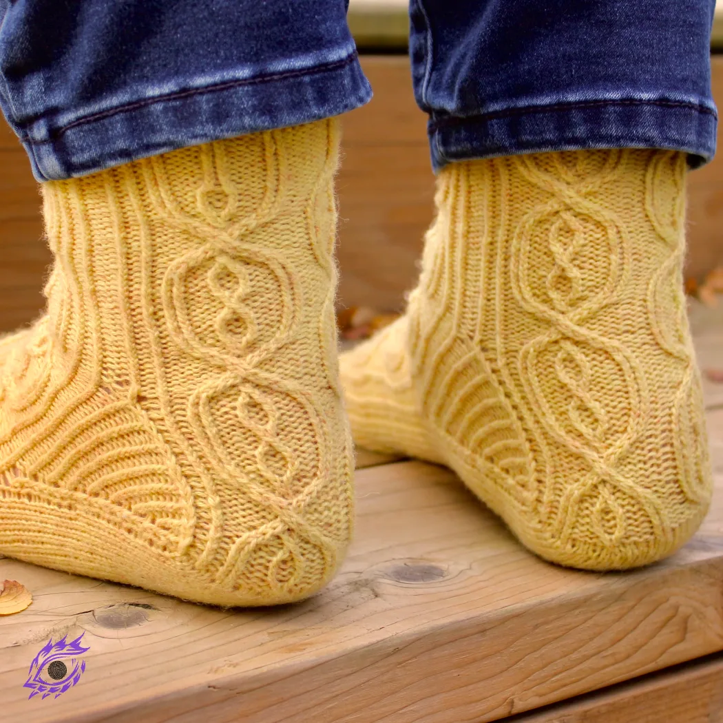 Back view of feet wearing yellow knitted socks with complex cable motif on heel flap and back of leg with twisted-rib accents.