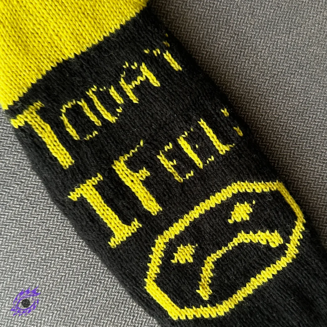Bottom view of yellow and black knitted socks with graphic sad face motif and text "Today I Feel".