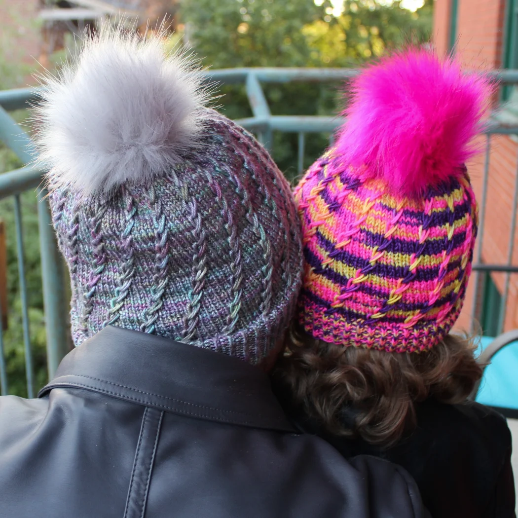 Back view of woman and child wearing toques with spiralling criss-crossing surface textures and coordinating pompoms.