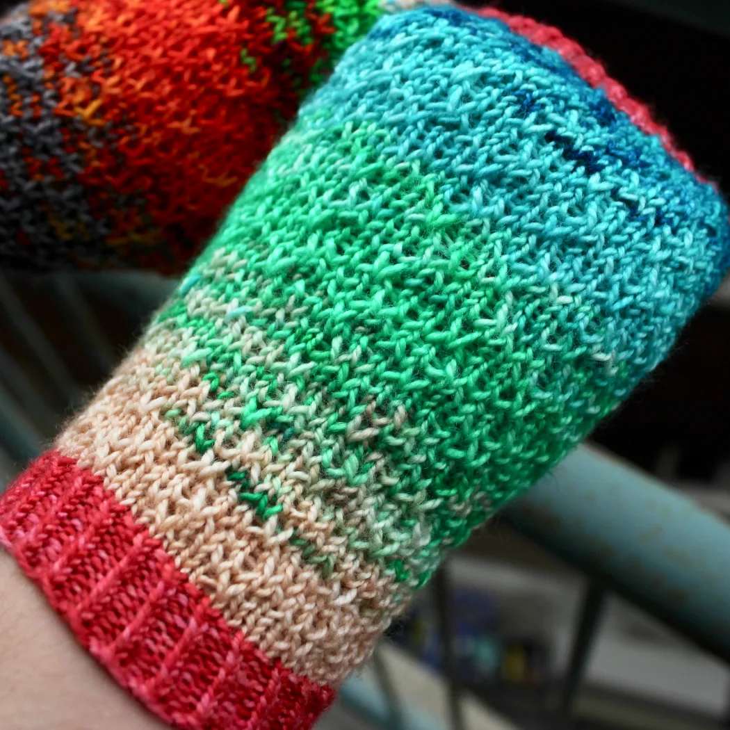 Close-up of mismatched multicoloured fingerless mitts with slipped-stitch texture.